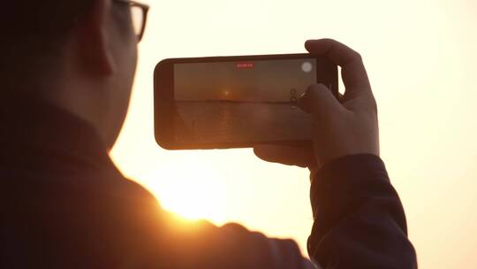 男人用手机拍摄海上日落美景