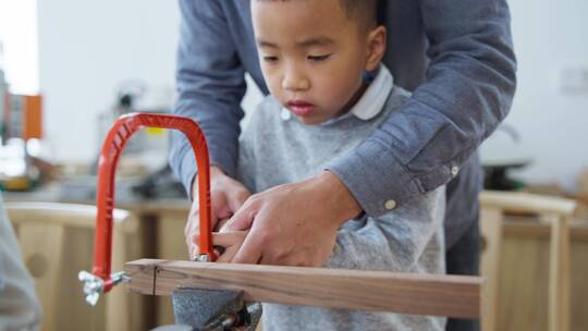 小男孩在老师指导下做木工锯木头动手能力