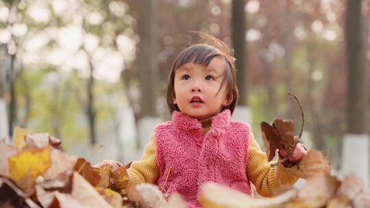 慢镜头特写小女孩坐在地上抛洒秋天的树叶