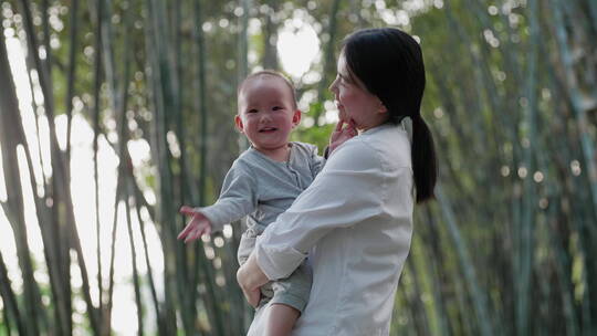 亚洲妈妈抱着快乐的小宝宝在春天的竹林公园