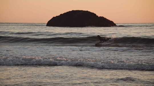 日落时在岩石海岸附近的海上冲浪的人