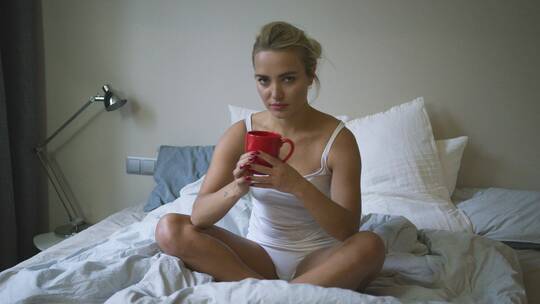 女人拿着水杯坐在床上