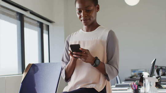 快乐的非裔美国女商人站着使用智能手机，在工作中微笑