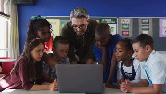 多样化的男老师和一群看着笔记本电脑的学童