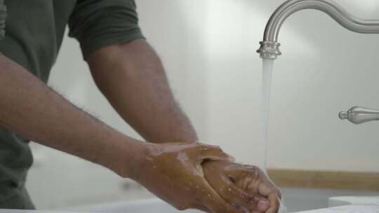男人在流动的水龙头下用肥皂水洗手