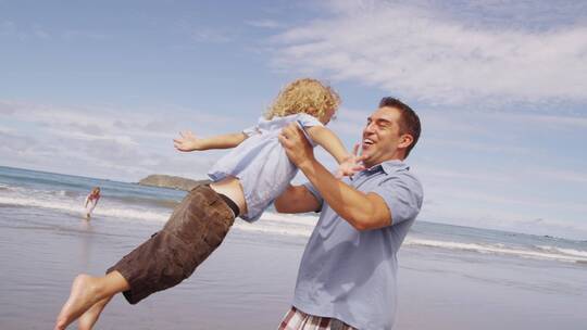 父亲在海边抱着孩子开心的转圈