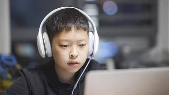 男孩子带着耳机使用笔记本电脑学习