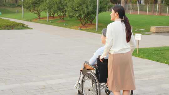 年轻女性推着坐轮椅的母亲公园散步