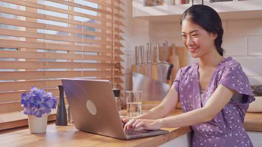 亚洲年轻女子在家中厨房使用笔记本电脑时喝视频素材模板下载