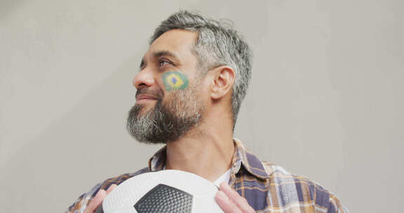 脸颊上插着巴西国旗的快乐混血儿拿着足球
