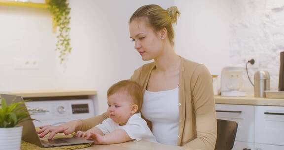 抱着孩子用笔记本电脑工作的女人