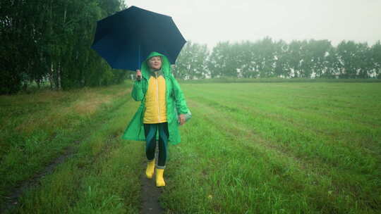 穿着绿色雨衣的女人在迷雾中行走时撑起雨伞