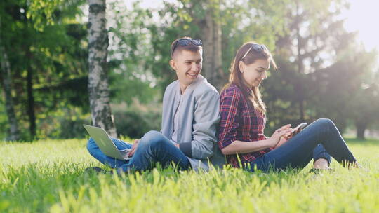 一男一女背靠背坐在草坪上玩手机