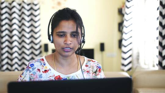 一名印度女人戴着耳机在家工作的特写镜头