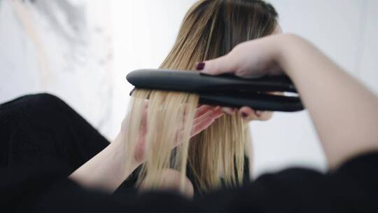 理发师用直板夹拉直女人的头发视频素材模板下载