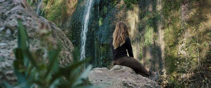 女人坐在山间石头上观赏瀑布