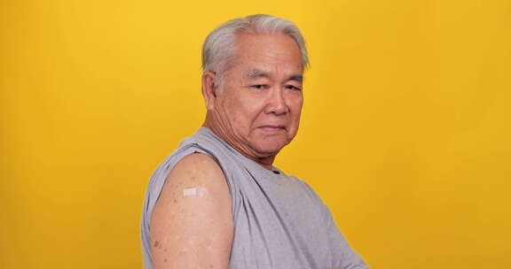 亚洲老人在接种疫苗后展示肩上的胶布绷带。