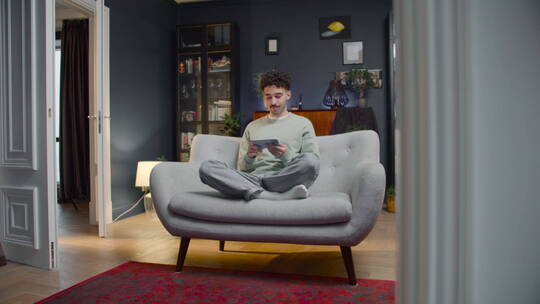 盘腿坐在沙发上玩手机的男人