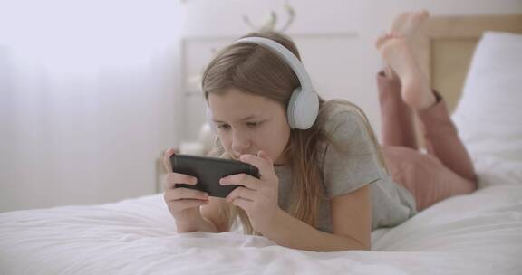 女人戴着耳麦趴在床上玩手机