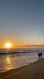 竖屏、黄昏时在沙滩上散步的情侣