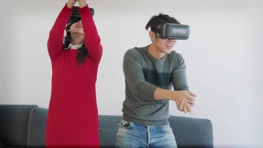 年轻的亚洲夫妇戴着VR眼镜在客厅玩耍。视频素材模板下载