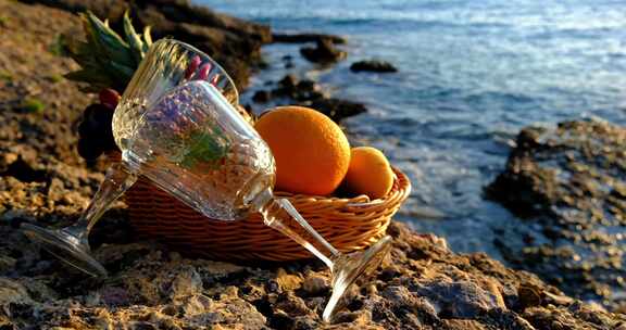 躺在海边的空酒杯跟水果篮橙子