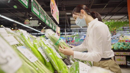 戴口罩的青年女人在超市选购蔬菜