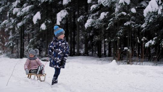 哥哥拉着坐在雪橇上的妹妹在雪地里行走视频素材模板下载