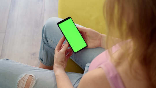 粉色上衣金发女郎手中拿着绿色屏幕色度键的手机后视图