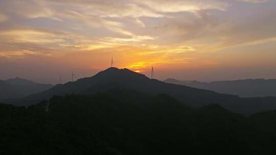 日落逆光时刻航拍群山山顶的大风车剪影