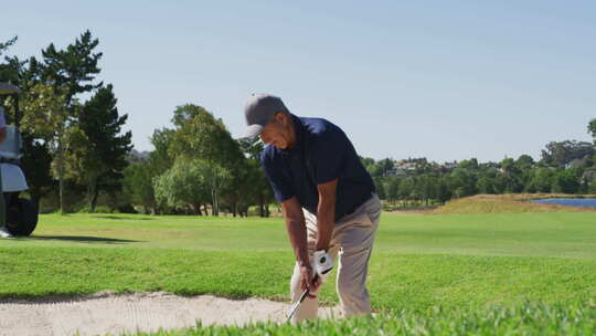阳光明媚的一天，高加索老人在高尔夫球场的沙坑里打高尔夫球