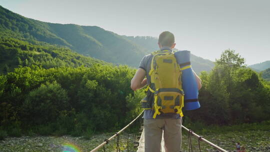 一个背着背包的旅行者沿着山河上摇摇晃晃的桥行走 