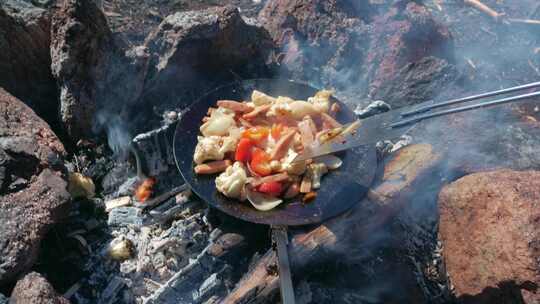 用铸铁平底锅和抹刀在篝火上烹饪食物。PO