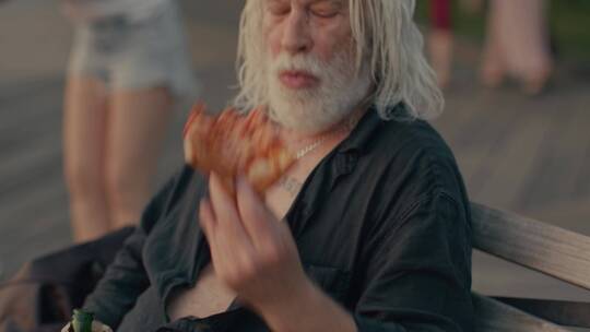 白发男人坐在街头吃披萨