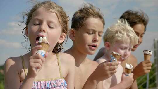 孩子们坐在微风和阳光下舔着冰淇淋甜筒