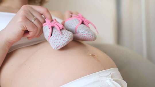 孕妇肚子上拿着婴儿鞋特写_4K视频素材模板下载