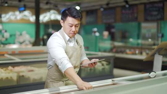 亚洲杂货店经理售货员在围裙使用数字平板电