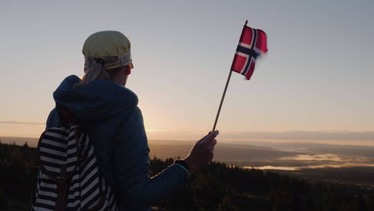一个手里拿着挪威国旗的旅行者在山顶遇见日出视频素材模板下载