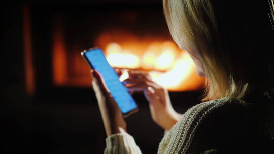 夜晚女人坐在壁炉旁玩智能手机