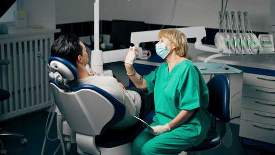 一名牙科诊所病人与一名拿着镜子咨询的女牙