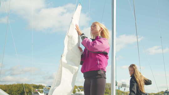 码头上的女子游艇队联合将主帆放在一艘白色运动游艇的桅杆上