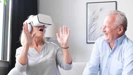 快乐的老人和女人在家戴着虚拟现实耳机坐在沙发上