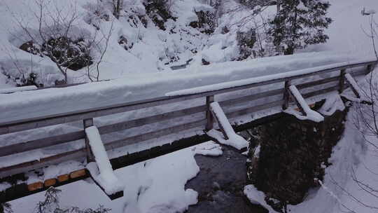 冬季仙境。阿尔卑斯山上有一条小溪的雪谷。无人机正在下降到一座桥前