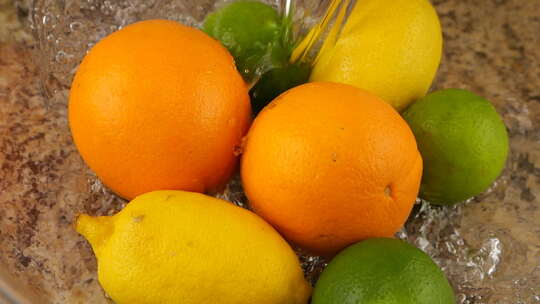 一股水流落在玻璃碗里的柑橘、橘子、柠檬和酸橙上。慢动作。视频素材模板下载