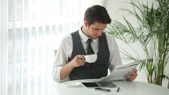 帅哥坐在桌边喝咖啡看报纸