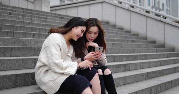 两位美女坐在台阶上看手机开心聊天