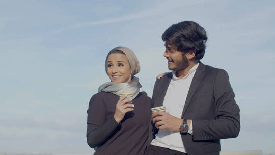 阿拉伯夫妇站在户外一边说话一边喝咖啡