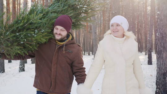 男人扛着圣诞树牵着妻子在森林