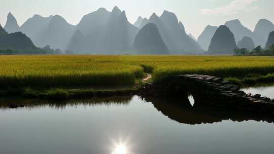 阳光下桂林山边小河上的石桥和岸边的稻田