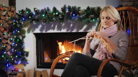 女人坐在为圣诞节装饰的壁炉旁编织衣服